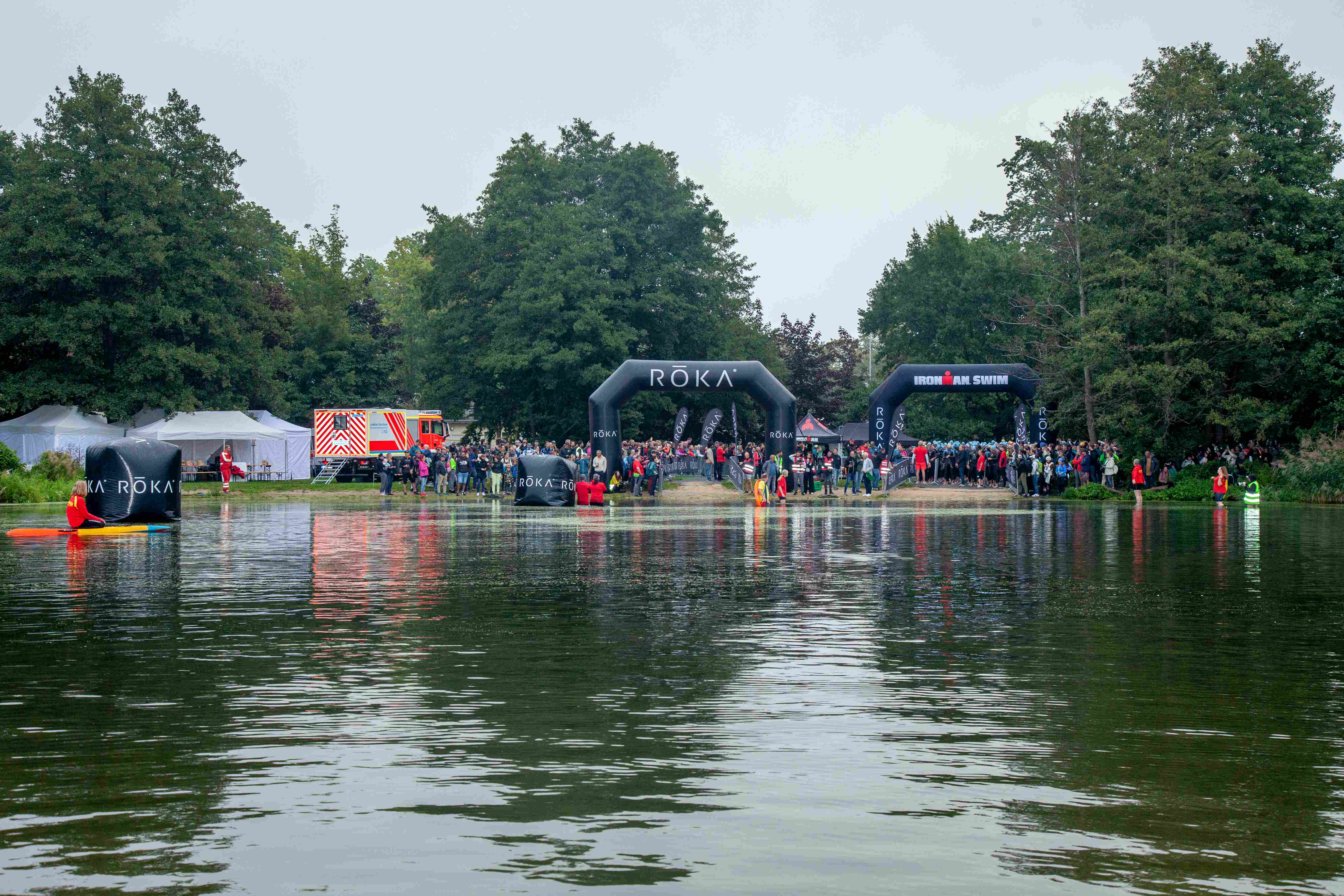 Der Start des Schwimmwettbewerbs steht unmittelbar bevor: Sportler:innen und Zuschauende haben sich bereits am Dämeritzsee eingefunden